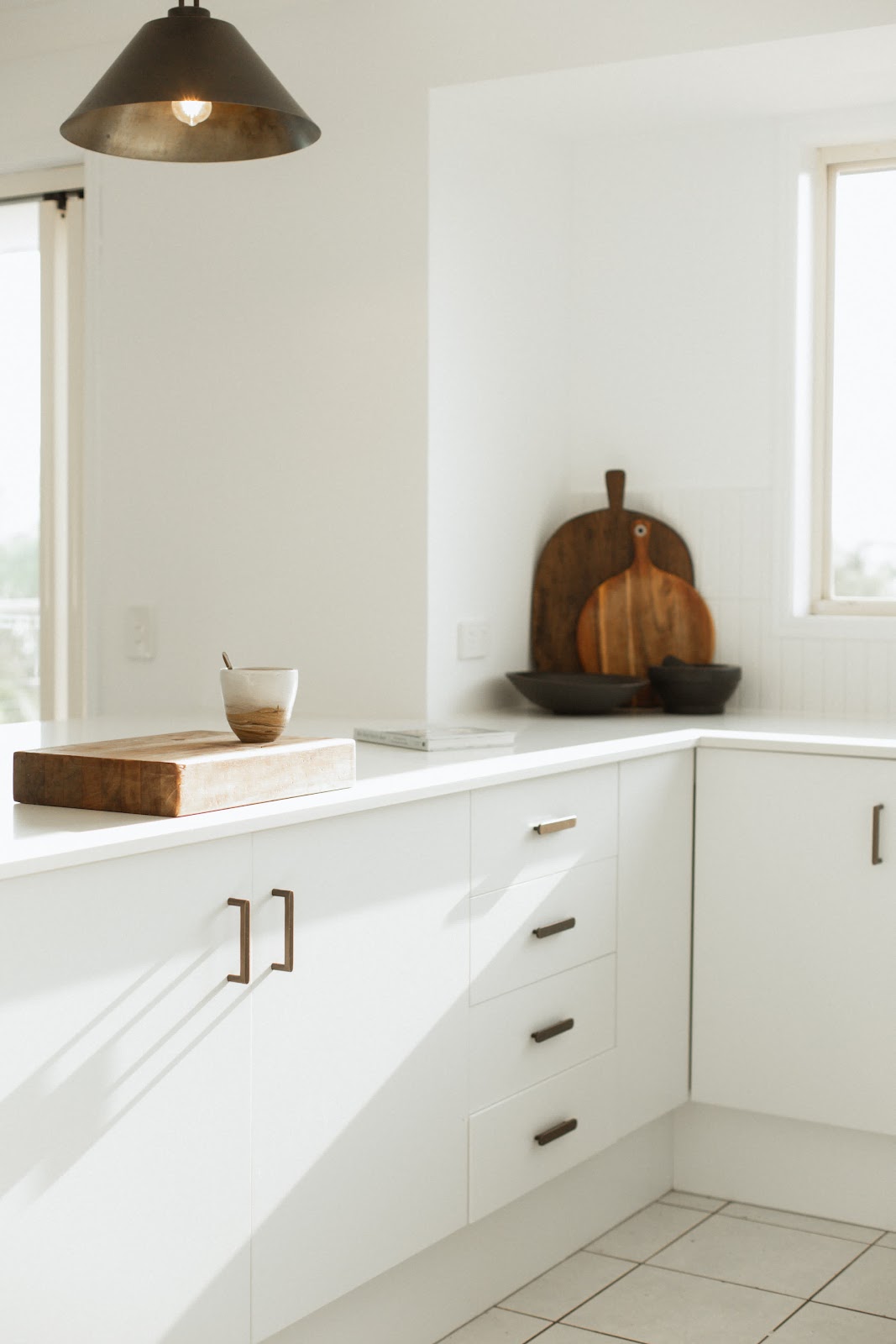 White shaker-style kitchen corner with brass handles, timber boards and a black pendant light