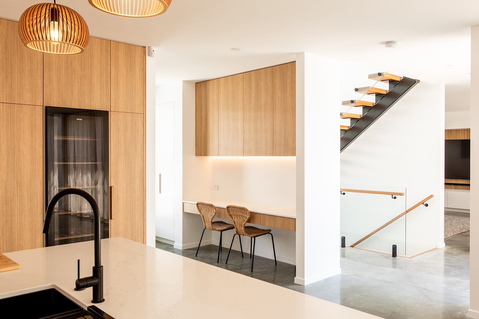 Timber-veneer tall cabinetry beside a white island with a black tap and a study nook behind
