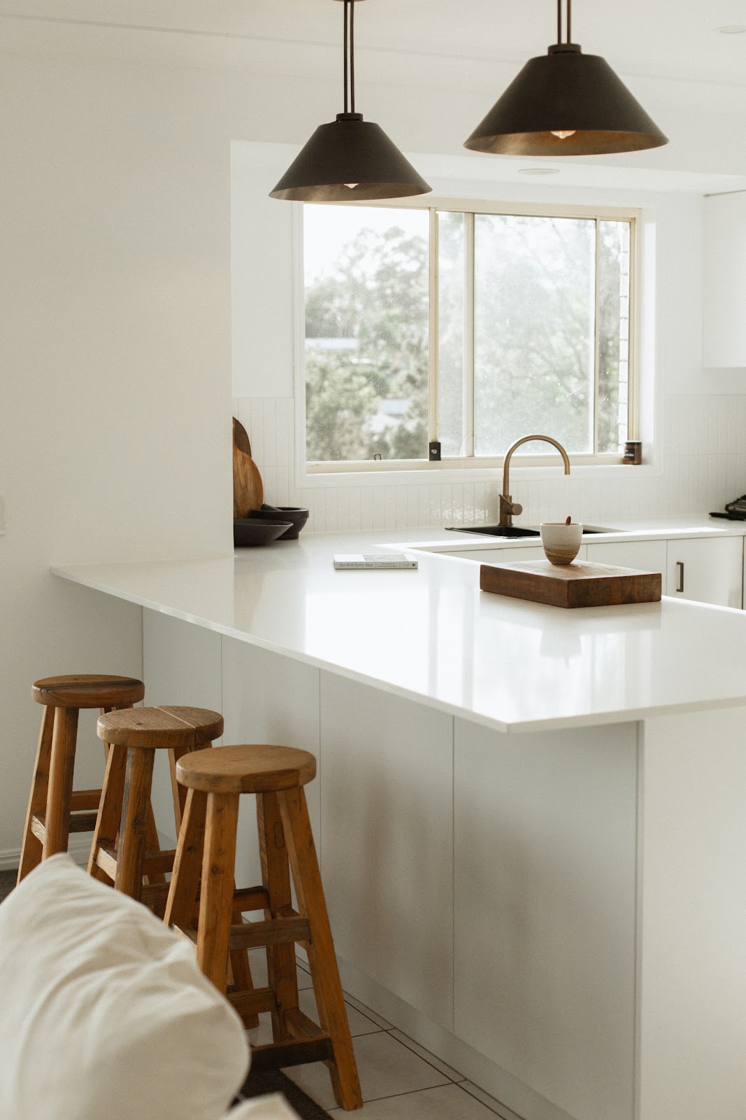 White kitchen peninsula with timber stools under black pendant lights